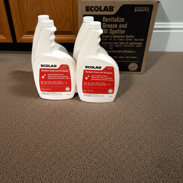 Two bottles of Ecolab Revitalize Grease and Oil Spotter on a carpeted floor with a cardboard box in the background.
