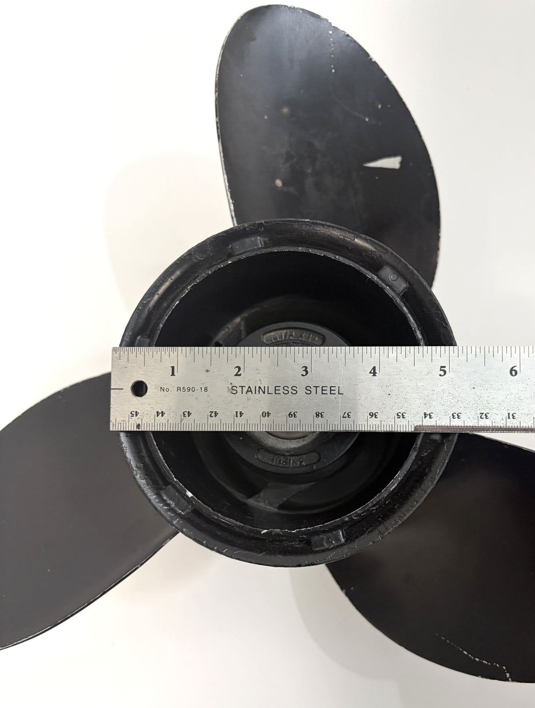 Top view of a pre-owned black Volvo aluminum propeller with three blades, featuring a stainless steel ruler measuring the 19-spline drive hub diameter.