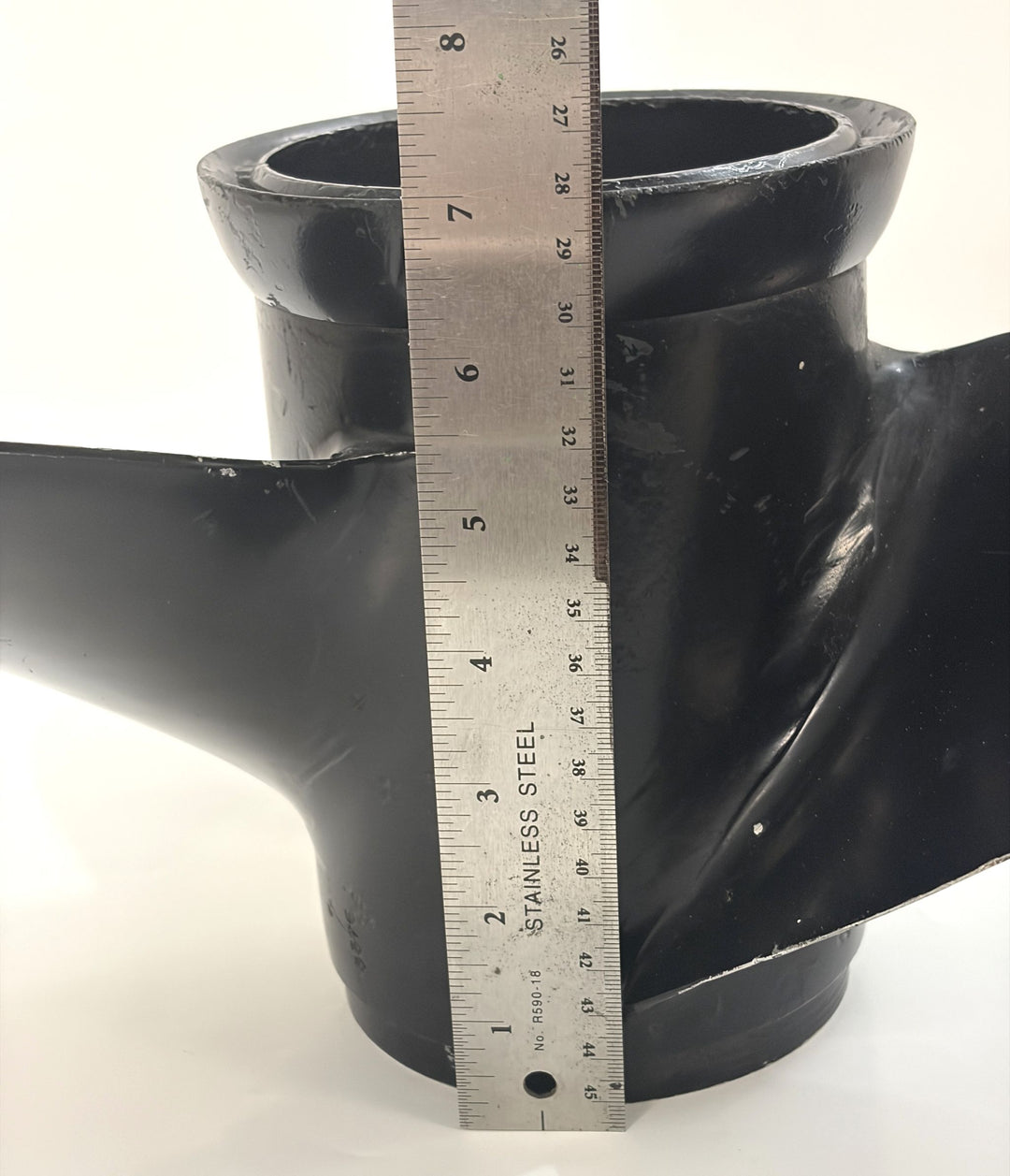 Close-up of a black metal propeller hub with a stainless steel ruler measuring its height, showing smooth edges and solid construction for marine use by Volvo.