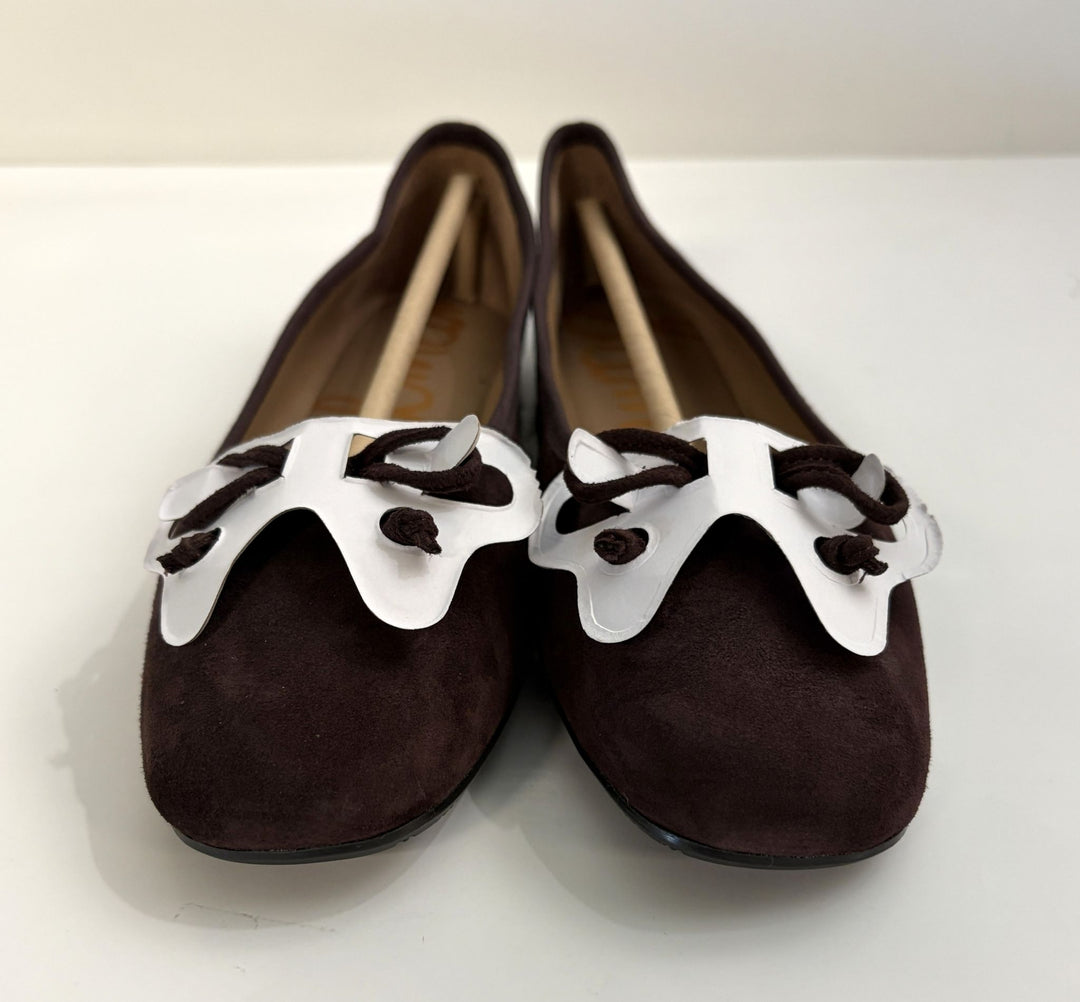 Pair of chocolate brown suede ballet flats by Sam Edelman featuring white bow accents and rounded toes, displayed on a plain white background.