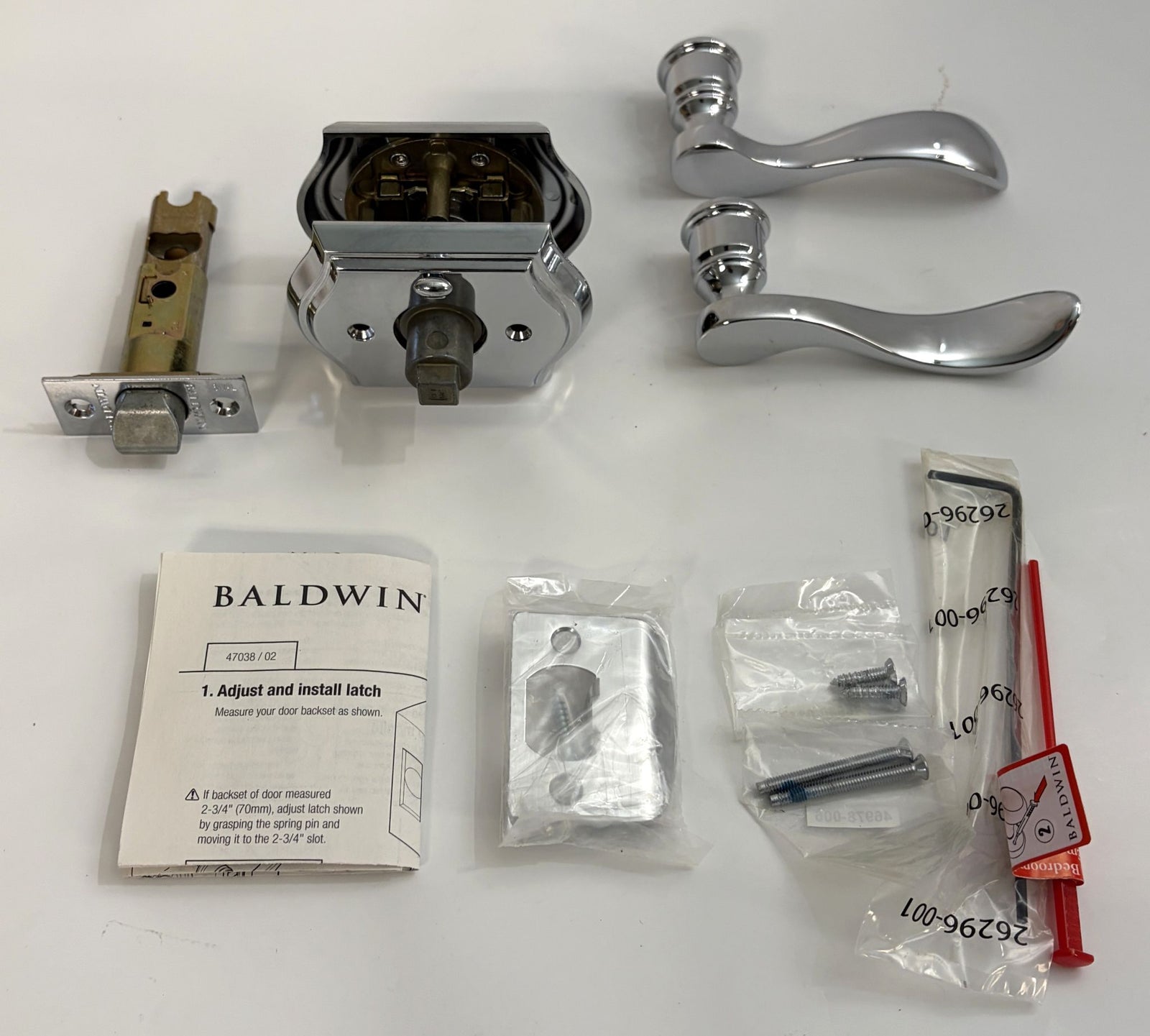 Baldwin privacy door lever set with curved chrome handles, latch mechanism, screws, installation instructions, and additional small hardware pieces displayed on a white background.