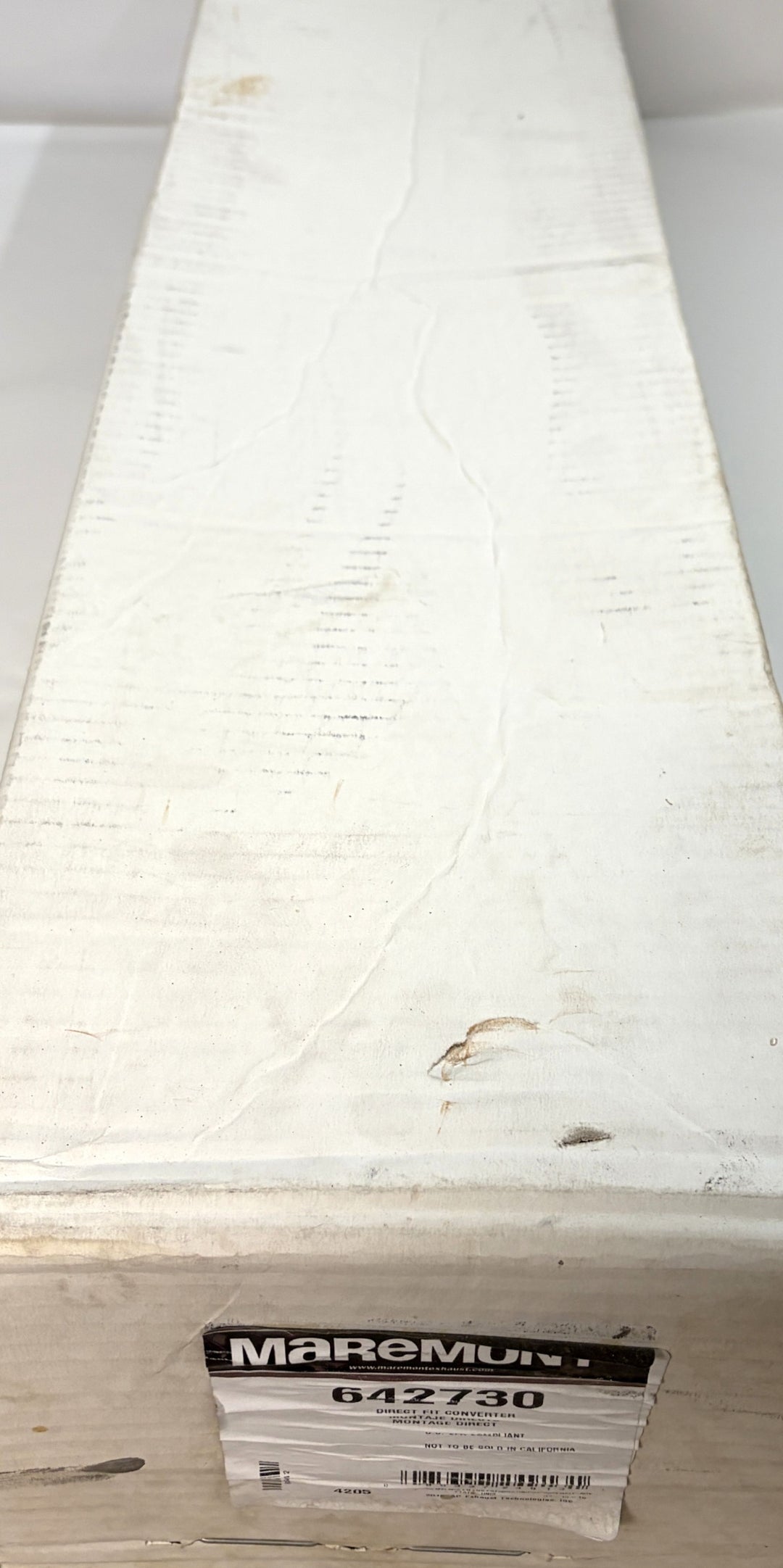 Long white cardboard box with visible creases and marks, featuring a worn label showing the Maremont brand and product number 642730 in an industrial warehouse setting.