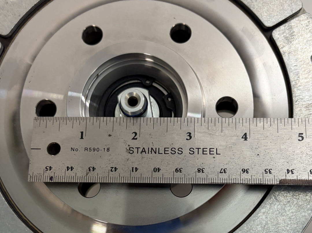 Close-up of a BorgWarner Kysor K32 rear air fan clutch showing stainless steel metal surface with mounting holes and a ruler measuring the diameter for size reference.