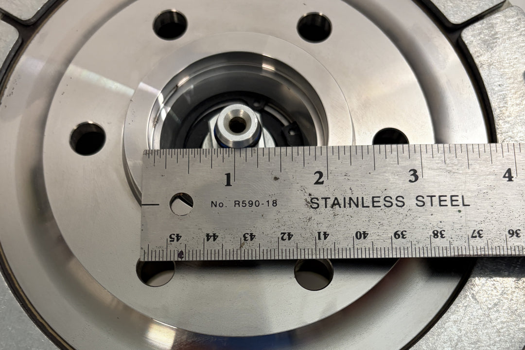 Close-up of a BorgWarner Kysor K32 rear air fan clutch showing central hub and mounting holes with a stainless steel ruler measuring its diameter on a metal surface.