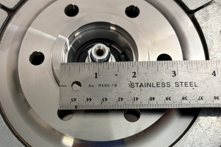 Close-up of a BorgWarner Kysor K32 rear air fan clutch showing central hub and mounting holes with a stainless steel ruler measuring its diameter on a metal surface.
