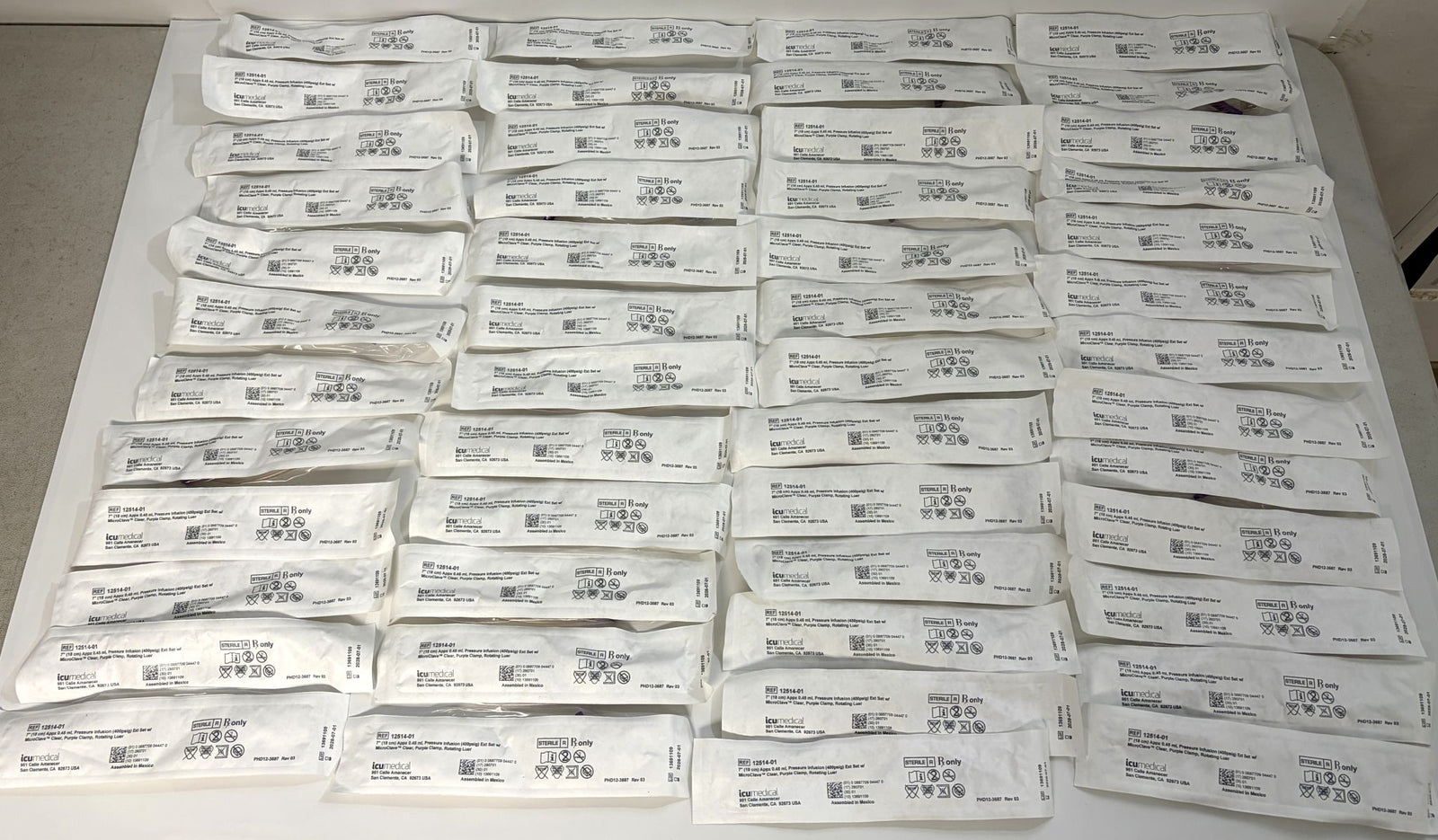 Multiple individually packaged ICU Medical pressure infusion extension sets neatly arranged on a flat surface, showcasing unopened medical supplies for clinical use.