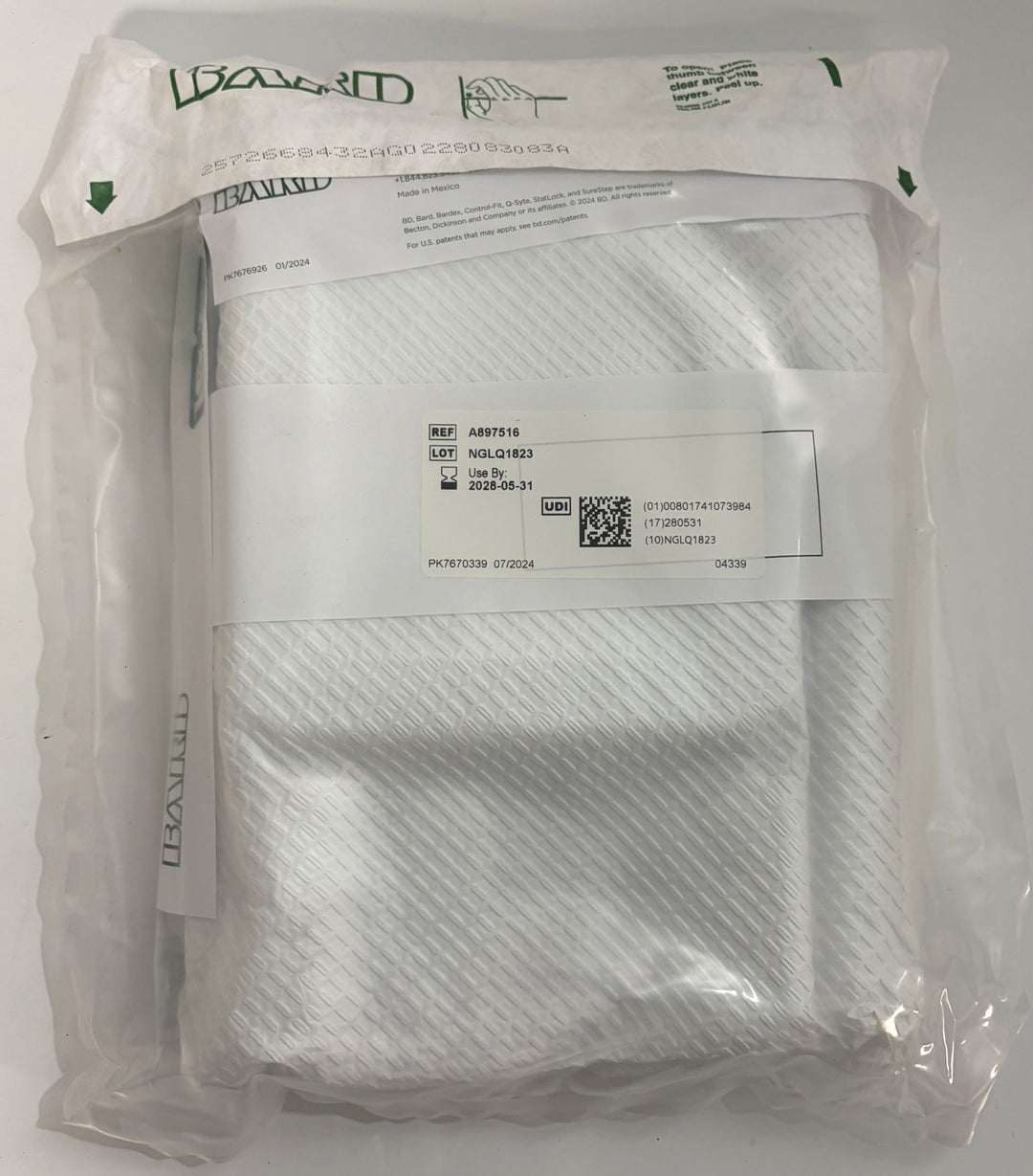 Sealed clear pouch containing a folded white medical dressing with a printed reference and lot number label