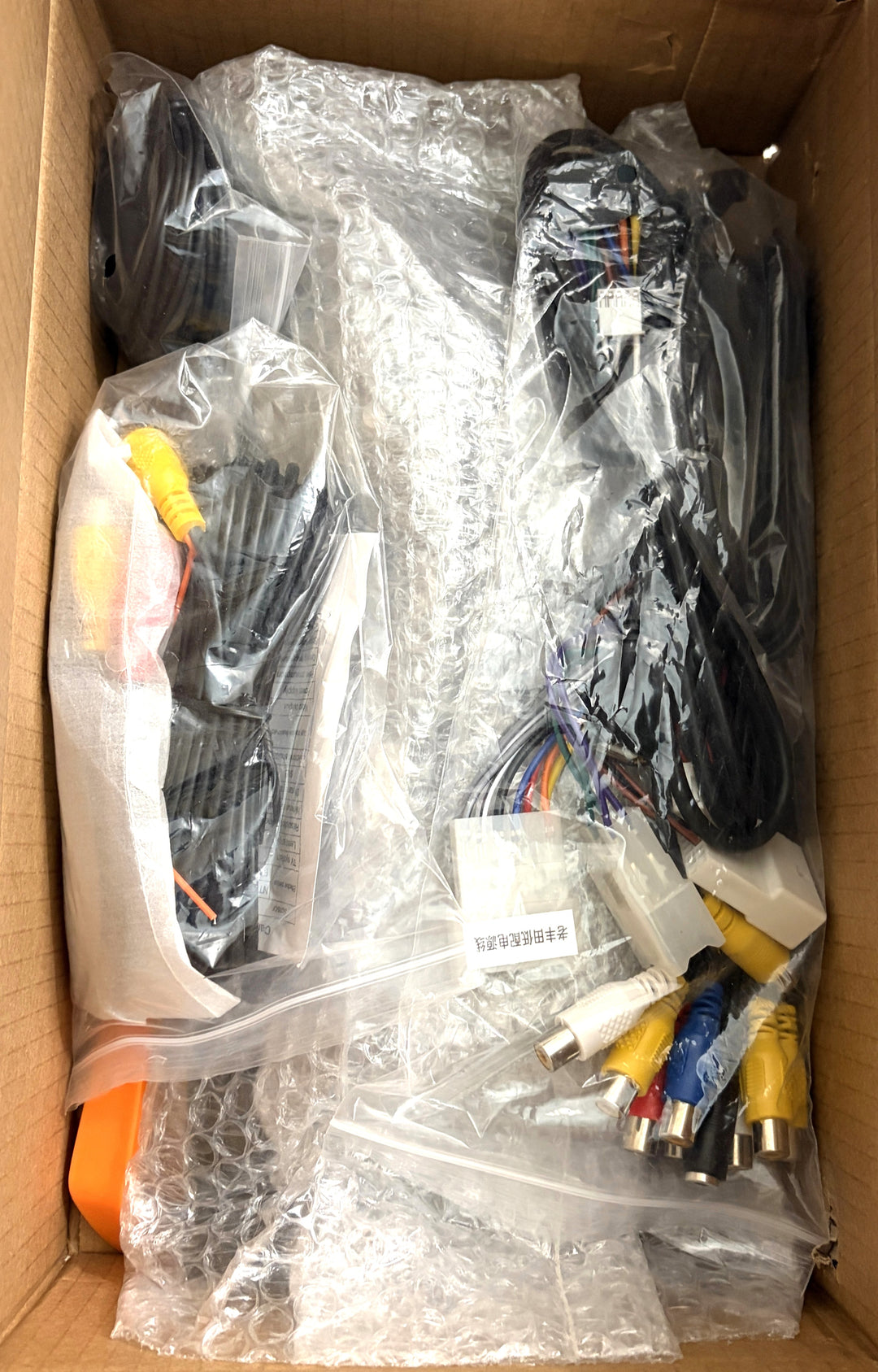 Open cardboard box containing assorted electronic cables, wiring harnesses, and multicolored audio video connectors wrapped in plastic and bubble wrap