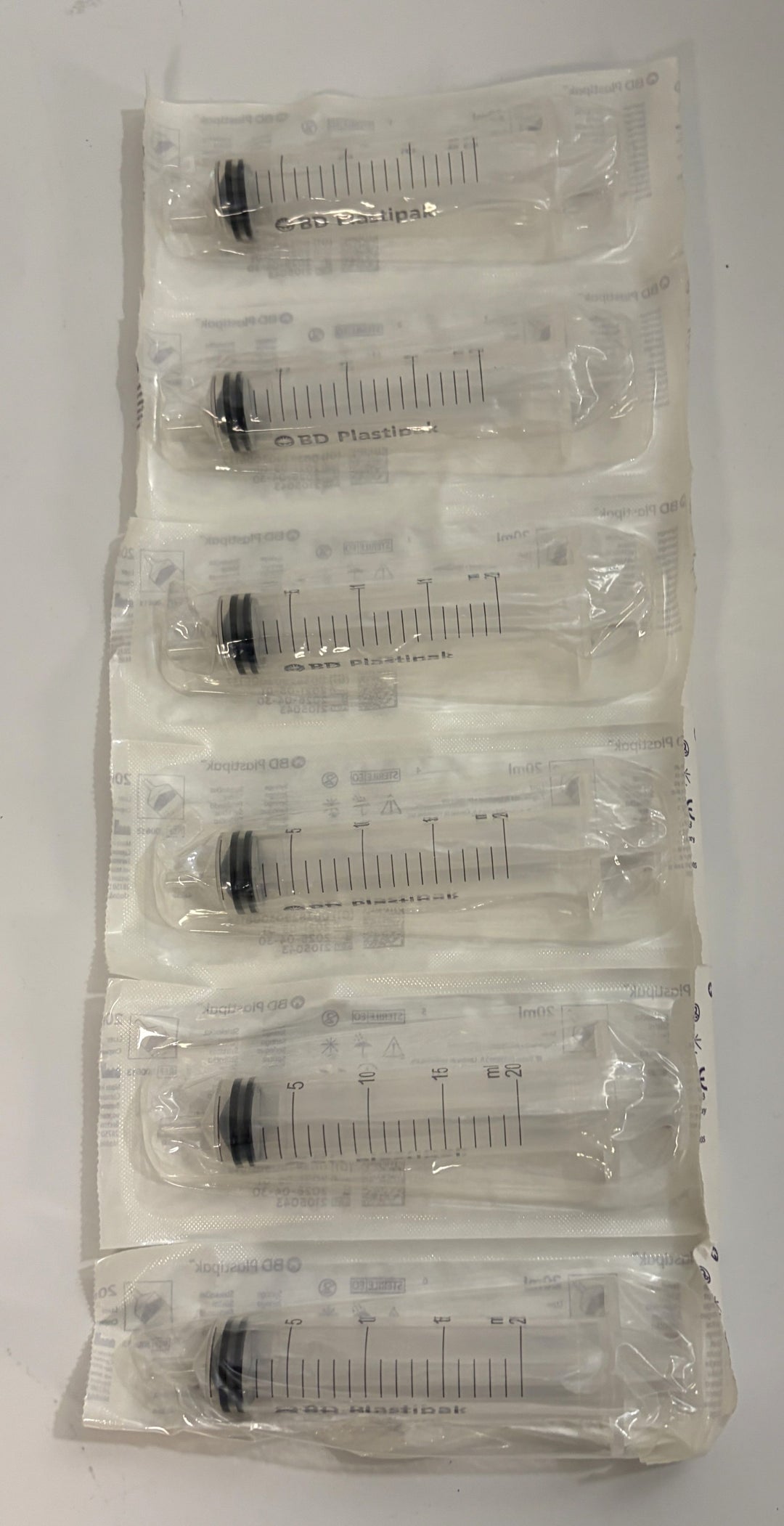 BD 20 mL Luer syringes individually sealed in clear plastic medical packaging, arranged in a stacked strip with graduated measurement markings