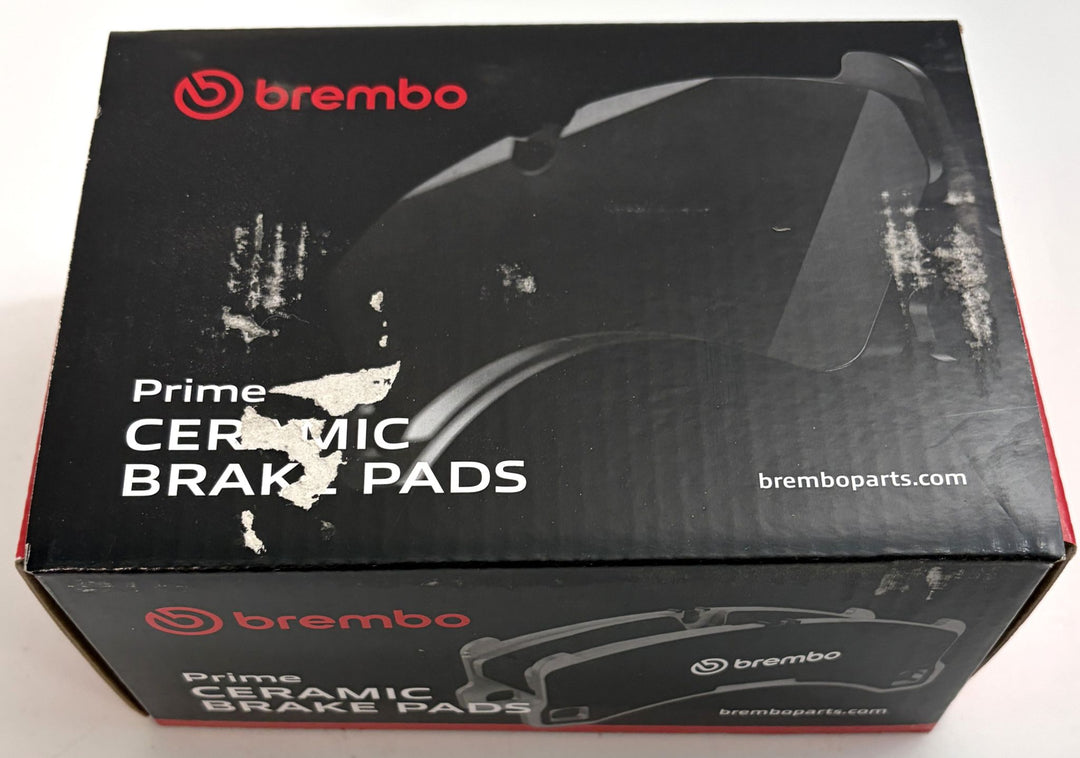 Brembo Prime ceramic brake pads box with black packaging, red branding, brake pad illustration, and visible scuffed and torn surfaces