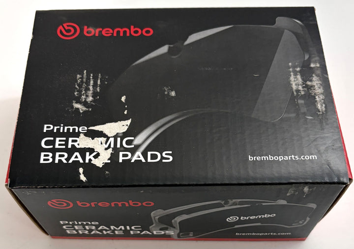 Brembo Prime ceramic brake pads box with black packaging, red branding, brake pad illustration, and visible scuffed and torn surfaces