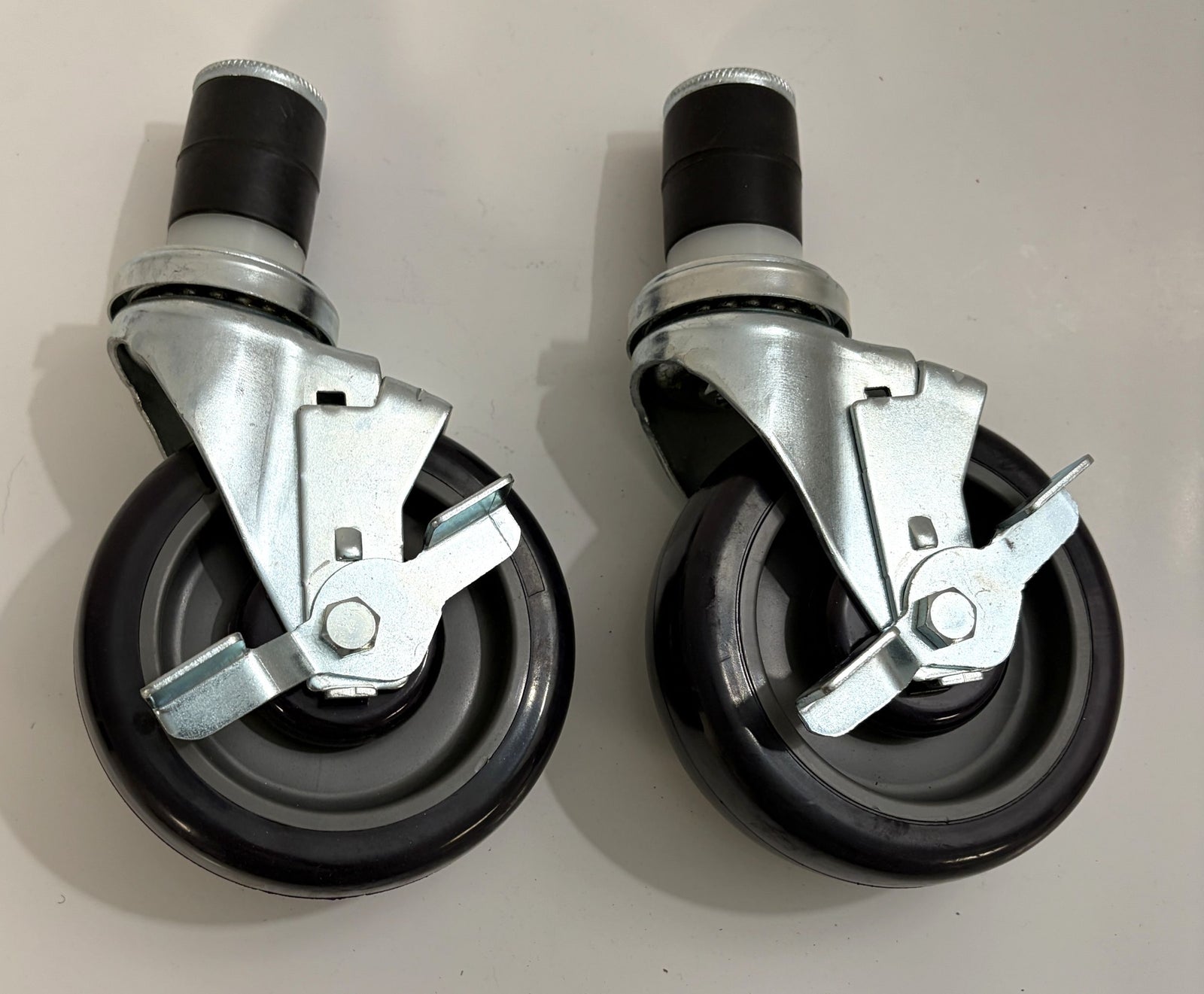 Two black caster wheels with metal brake mechanisms on a light gray background