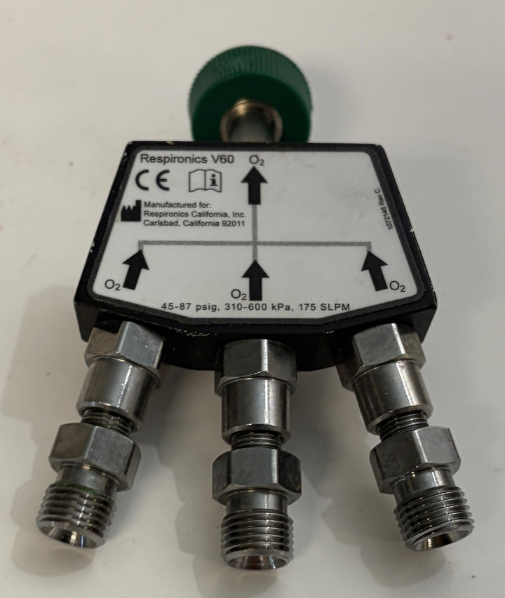 Respironics V60 O2 oxygen manifold with three threaded metal fittings and a green rear connector on a white surface