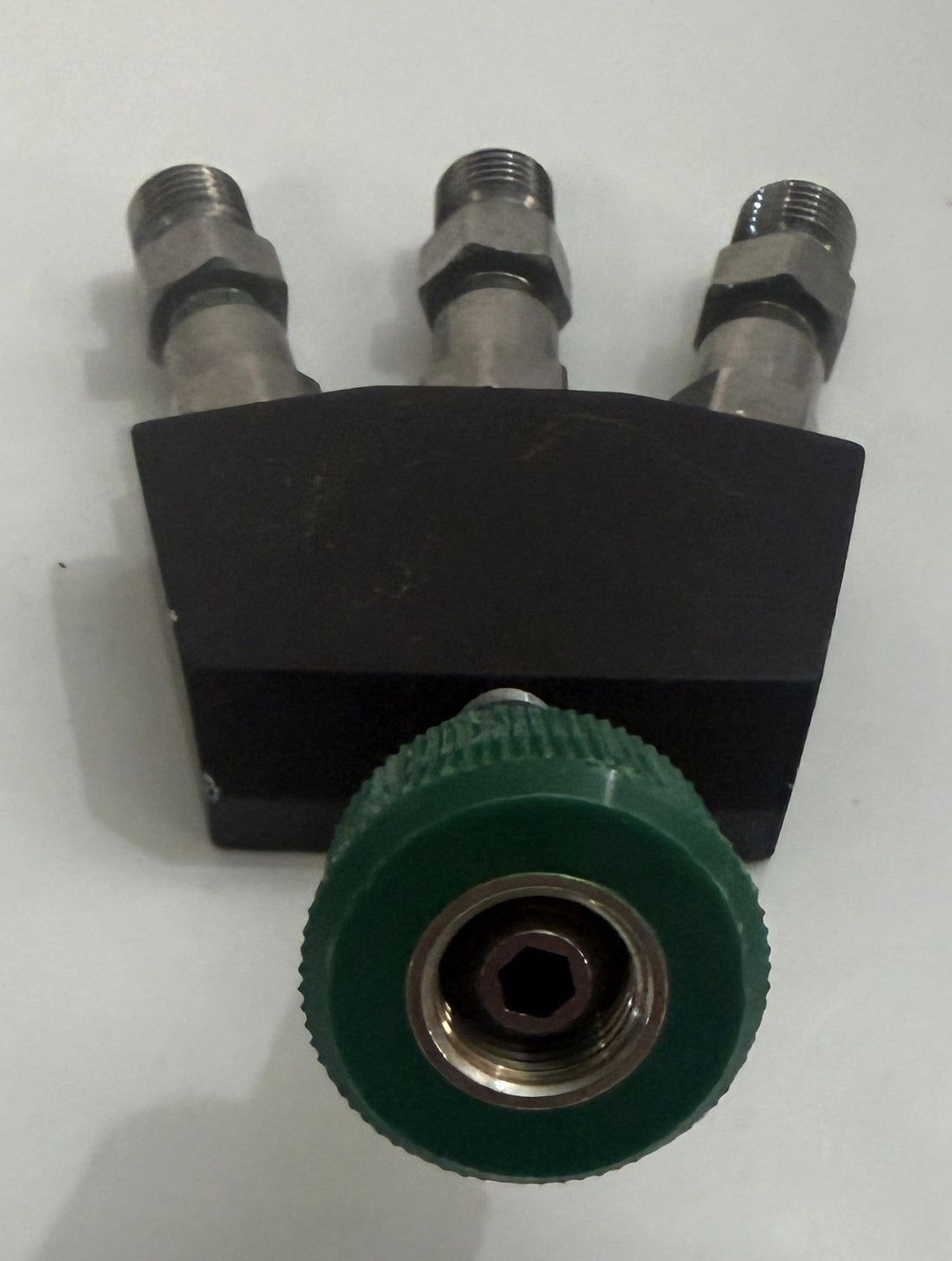 Black metal three-port valve assembly with three threaded fittings and a large green ridged adjustment knob on a white background