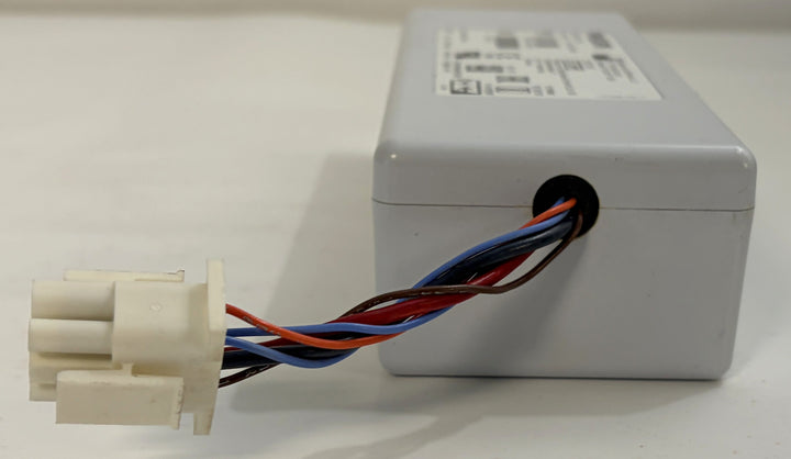 Gray electrical control module with red, blue, and black wires leading to a white multi-pin connector on a light surface.