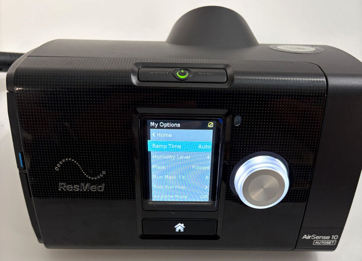 ResMed AirSense 10 AutoSet CPAP console in black, powered on with menu screen, control dial, and illuminated power button