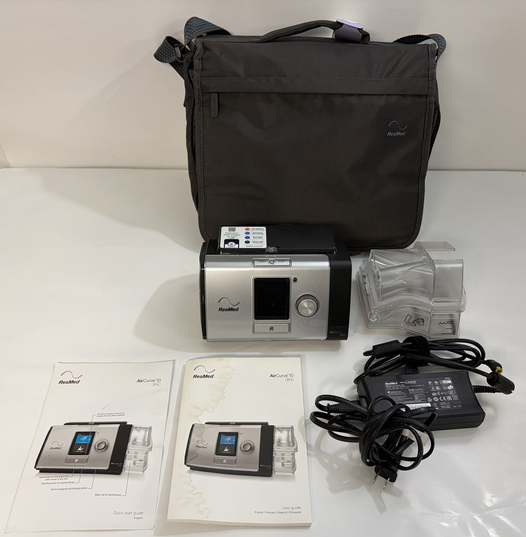ResMed CPAP machine with black carrying case, clear humidifier chamber, power adapter, and instruction manuals arranged on a white surface
