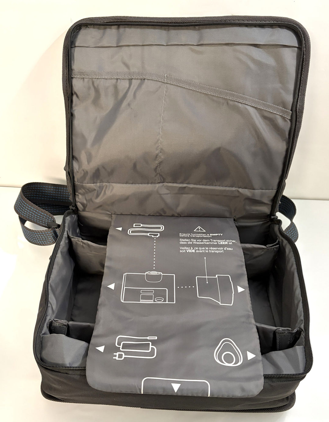 Open black and gray padded carrying case with multiple compartments, shoulder strap, and an illustrated instruction panel inside the lid.