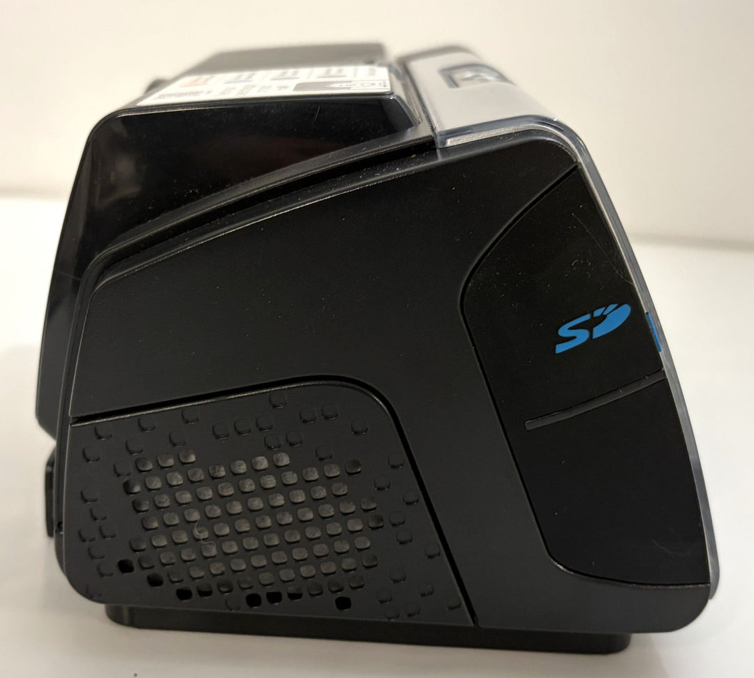 Black electronic desktop device with a blue stylized logo, angular housing, top control panel, and textured side speaker-like panel.