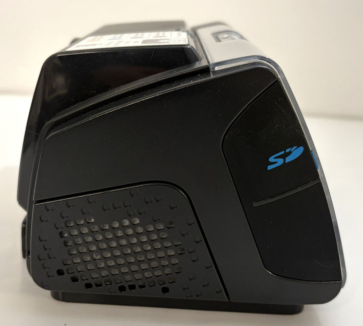 Black electronic desktop device with a blue stylized logo, angular housing, top control panel, and textured side speaker-like panel.
