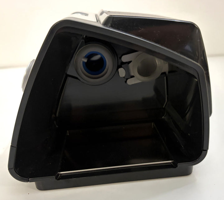 Black plastic housing with an open rectangular compartment, circular blue-lined opening, and adjacent round port against a white background.