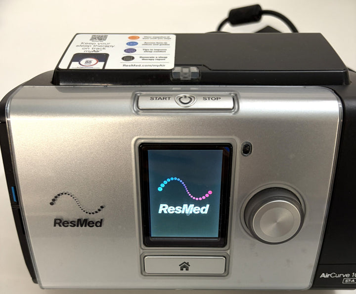 ResMed AirCurve sleep therapy machine with silver and black housing, control dial, touchscreen showing the ResMed logo, and start stop buttons