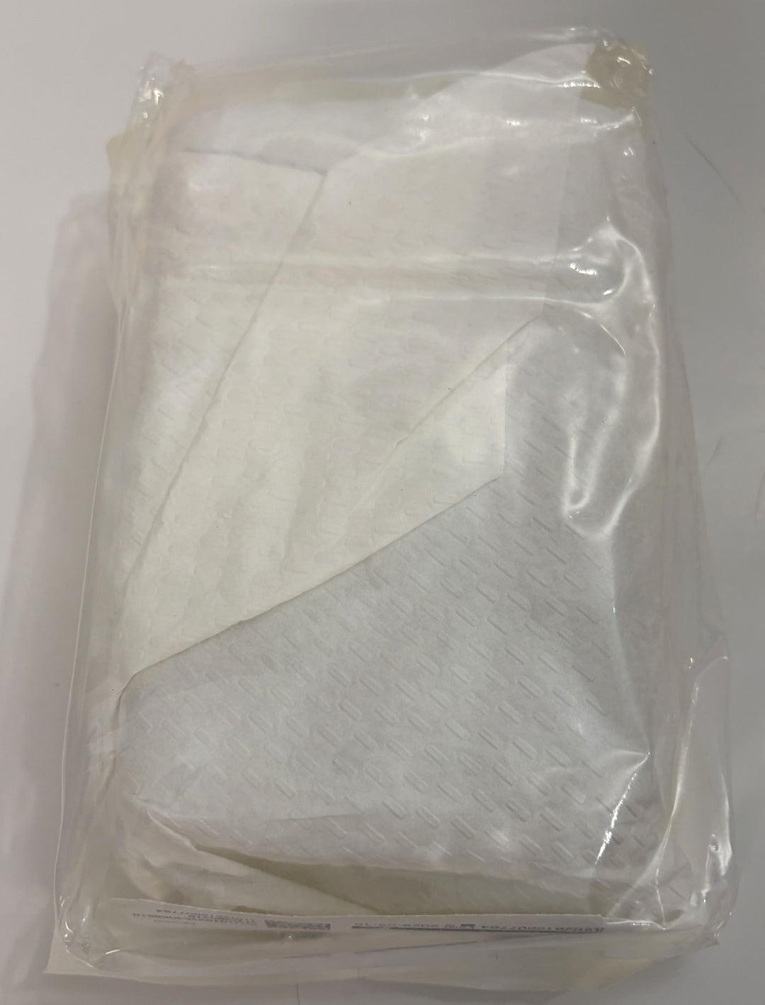Sealed clear plastic package containing folded white textile material with a soft, layered appearance.