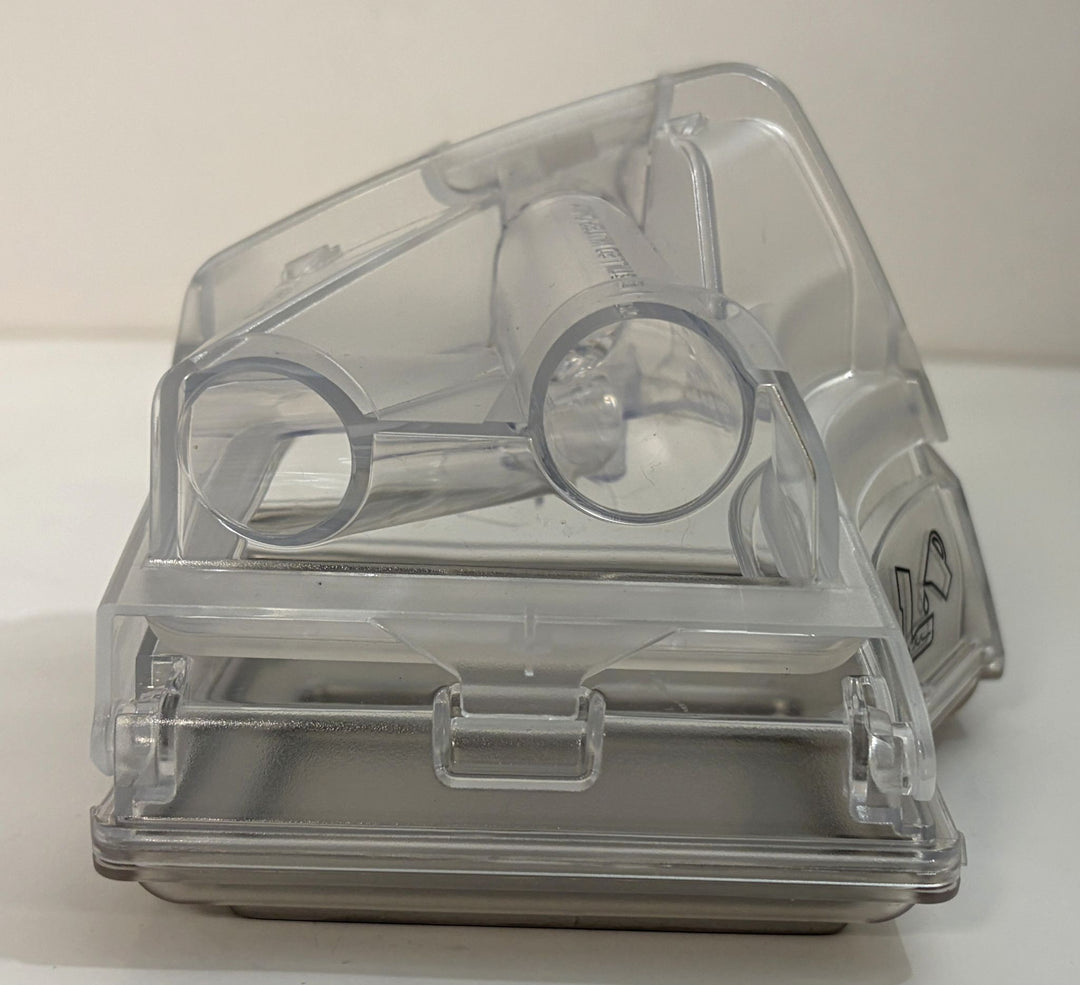Clear plastic enclosed device with two circular openings, internal components, side safety symbol, and a front latch on a white surface
