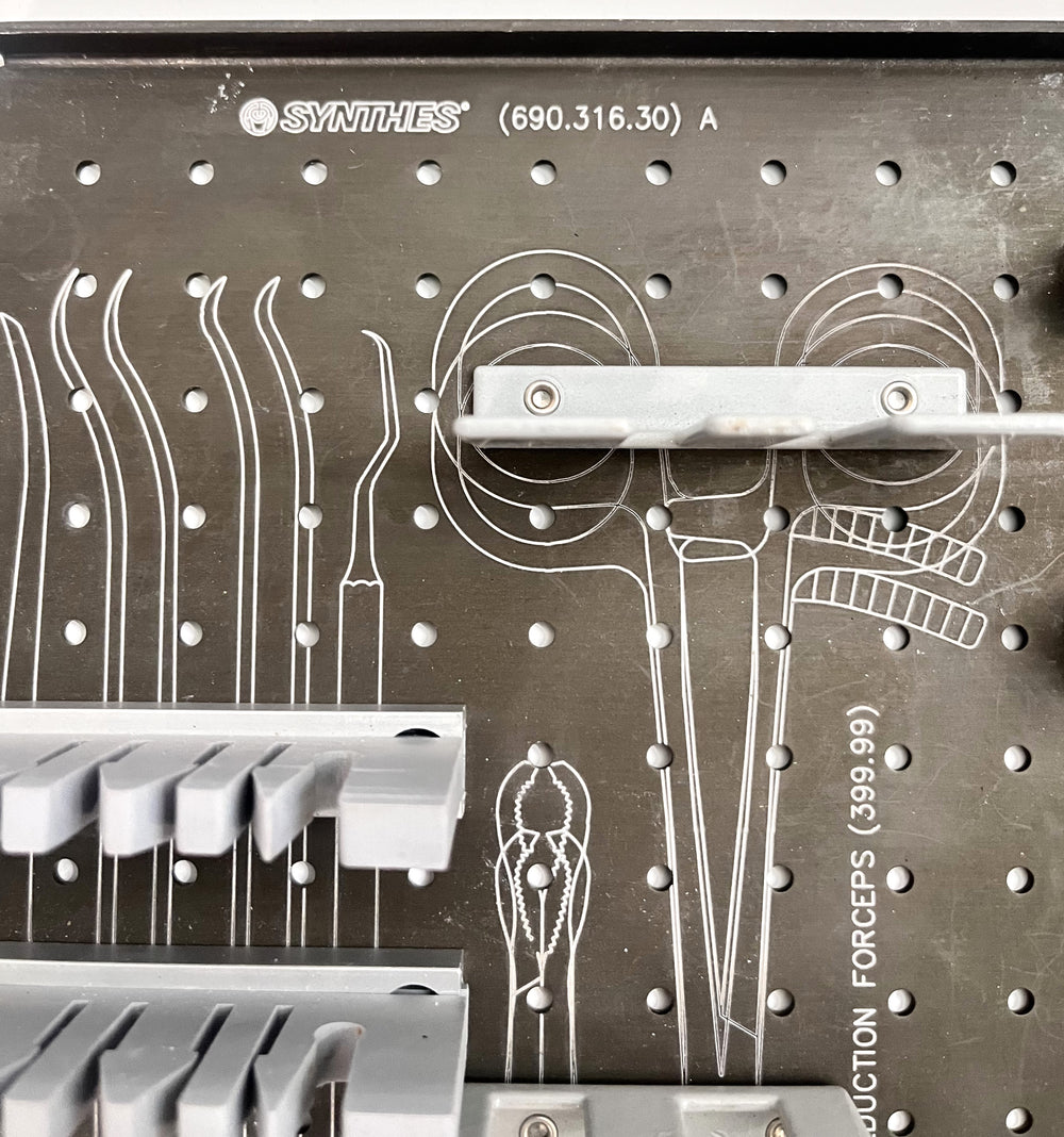 Stainless steel Synthes instrument tray with organized compartments for surgical tools, used in orthopedic and trauma procedures.