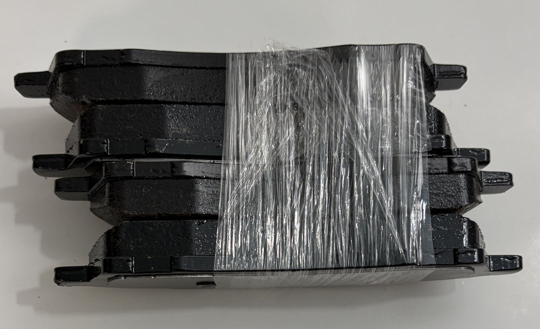 Set of four black Akebono ceramic brake pads stacked and wrapped in clear plastic against a white background, showing the smooth friction surface and mounting tabs.