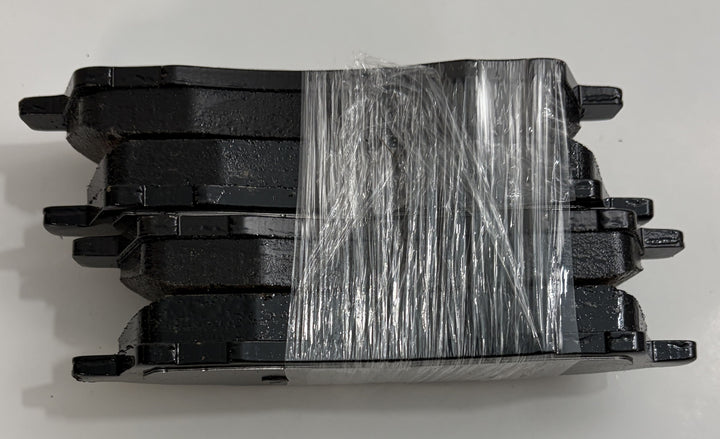 Set of four black Akebono ceramic brake pads stacked and wrapped in clear plastic against a white background, showing the smooth friction surface and mounting tabs.