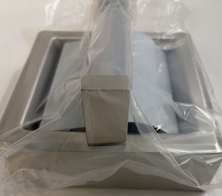 Close-up of a satin finish toilet paper holder with hood and frame by ASI, partially wrapped in protective plastic packaging on a neutral background.