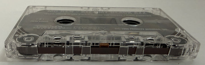 Close-up of a clear plastic audio cassette tape with visible magnetic tape inside, representing a pre-owned music item available from Priority Records.