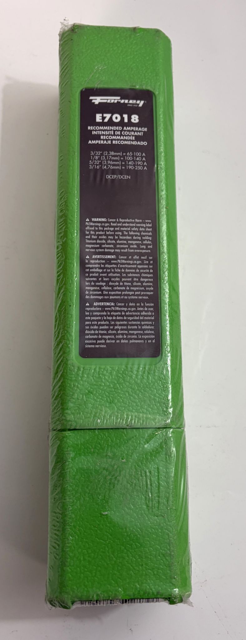 Green rectangular package of Forney E7018 welding electrodes with detailed amperage recommendations and safety warnings visible on the front label against a plain background.