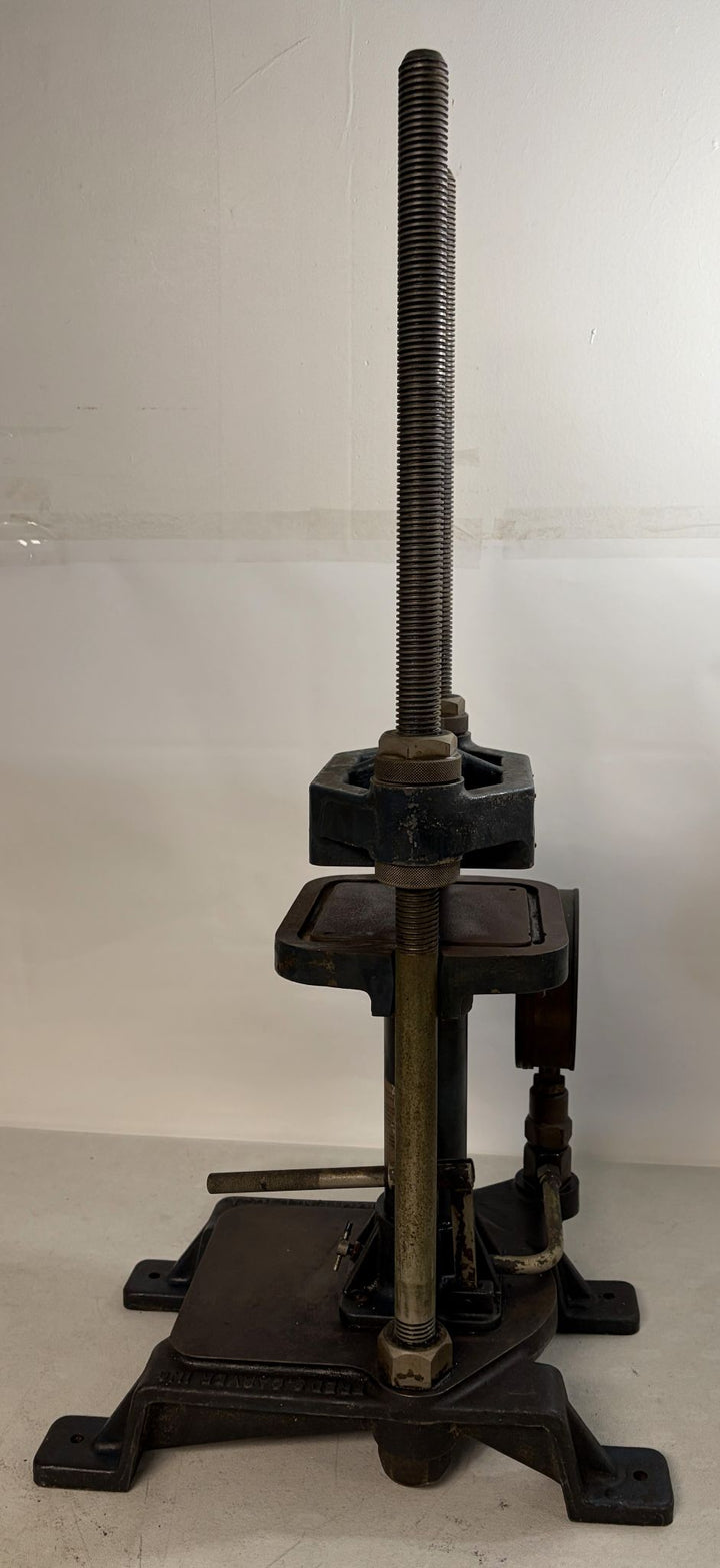Pre-owned heavy-duty hydraulic bench press with threaded vertical screw, cast iron base, and adjustable clamp components, manufactured by Carver Inc for industrial use.