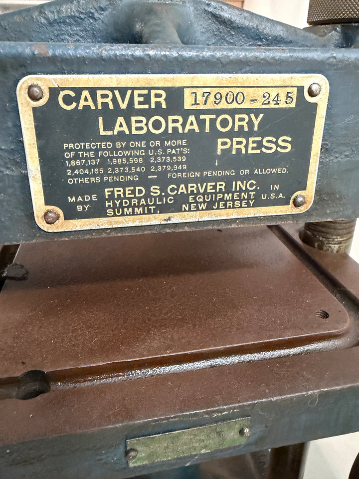 Close-up of the identification plate on a Carver Inc hydraulic laboratory press showing model number 17900-245 and patent information on a metal surface.