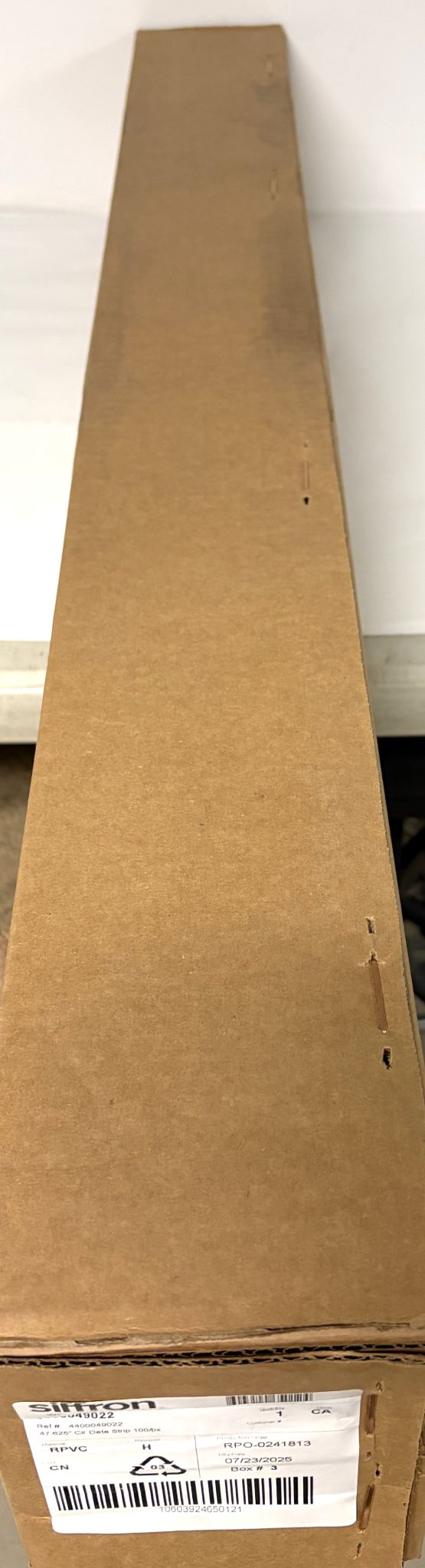 Long rectangular plain brown cardboard box with a white shipping label on one end, containing Siffron clear shelf label holders for business or industrial use.