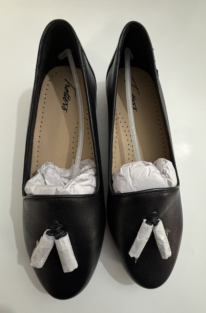 Pair of black leather tassel loafers with beige cushioned insoles and protective white paper stuffing, displayed from a top view on a white surface.