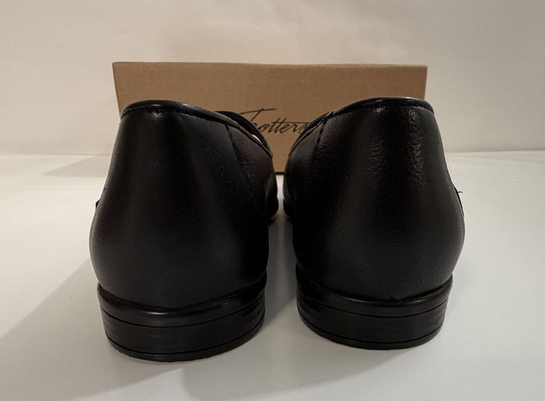 Pair of black leather loafers with tassel detail shown from the back, displayed on a white surface with a branded cardboard box in the background.