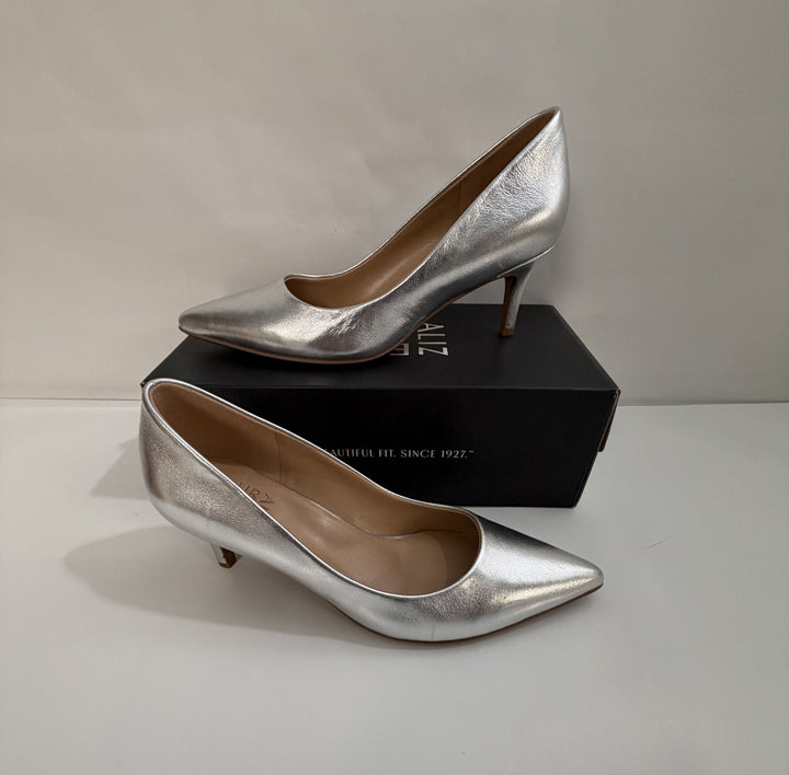 Pair of metallic silver pointed-toe high heels with kitten heels displayed on and beside a black shoebox against a neutral background.