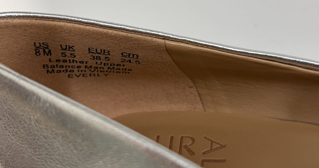Close-up of the inside heel area of a metallic silver shoe showing size markings and material information on the leather upper lining.