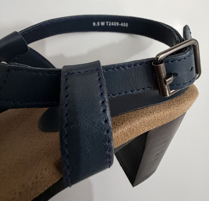 Close-up view of a navy leather strap and adjustable buckle on a Trotters sandal featuring a cushioned tan insole and a tapered block heel.