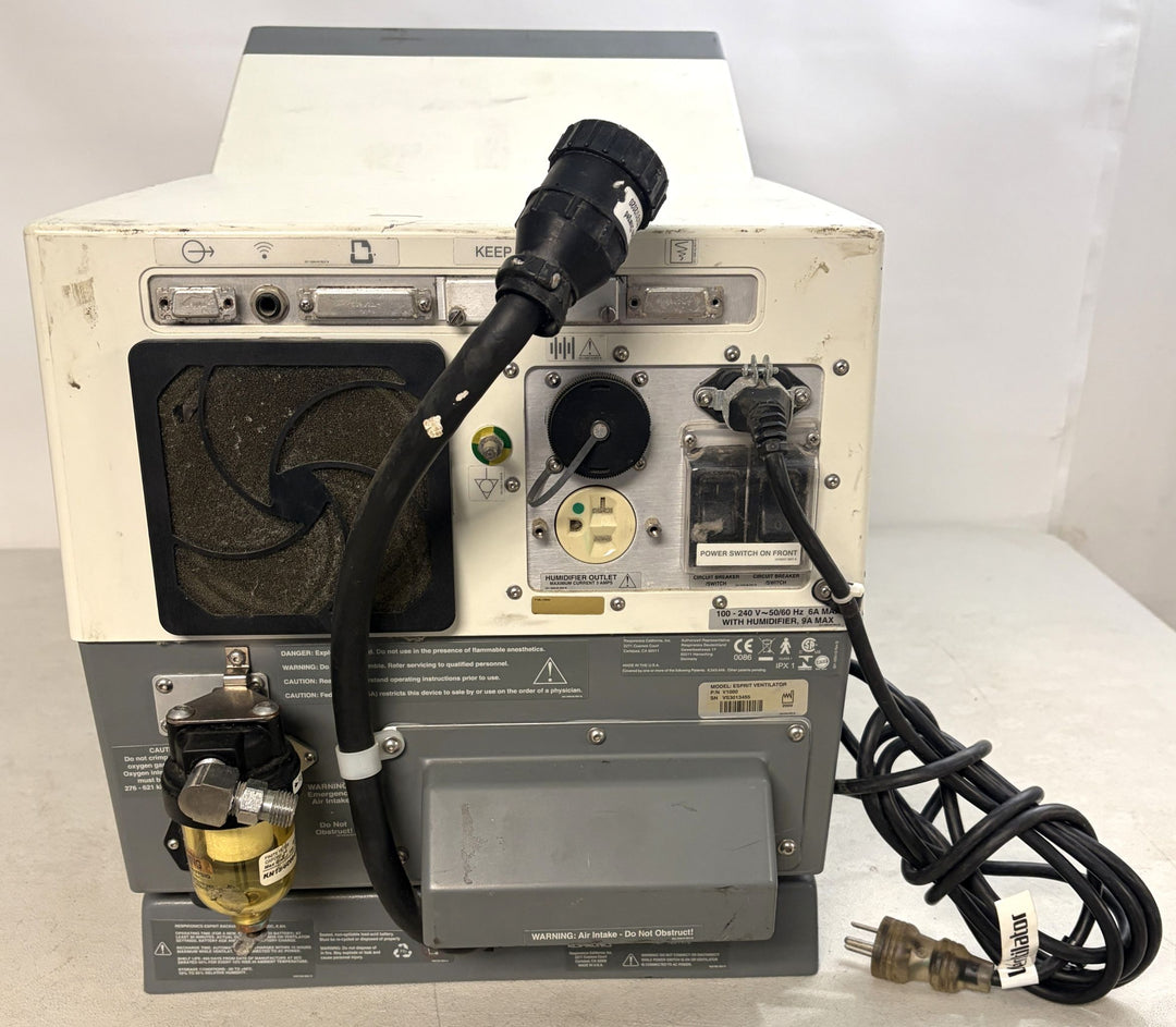 Rear view of a used Philips Respironics medical device core unit showing ventilation fan, power inlet, attached cables, and connector ports on a white surface.