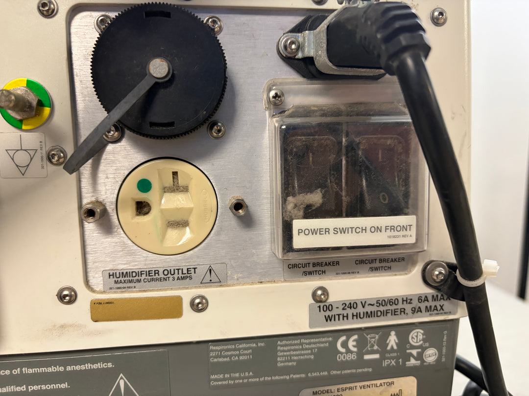 Close-up view of the control panel on a Philips Respironics device showing a humidifier outlet, power switch label, circuit breakers, and connected black power cord.