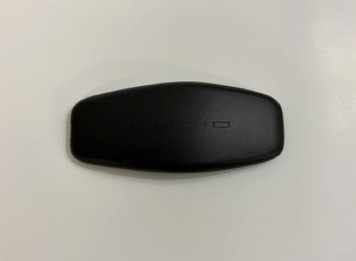Close-up of a black Lucid key fob for keyless entry, showing smooth matte surface with subtle branding on a plain light background.