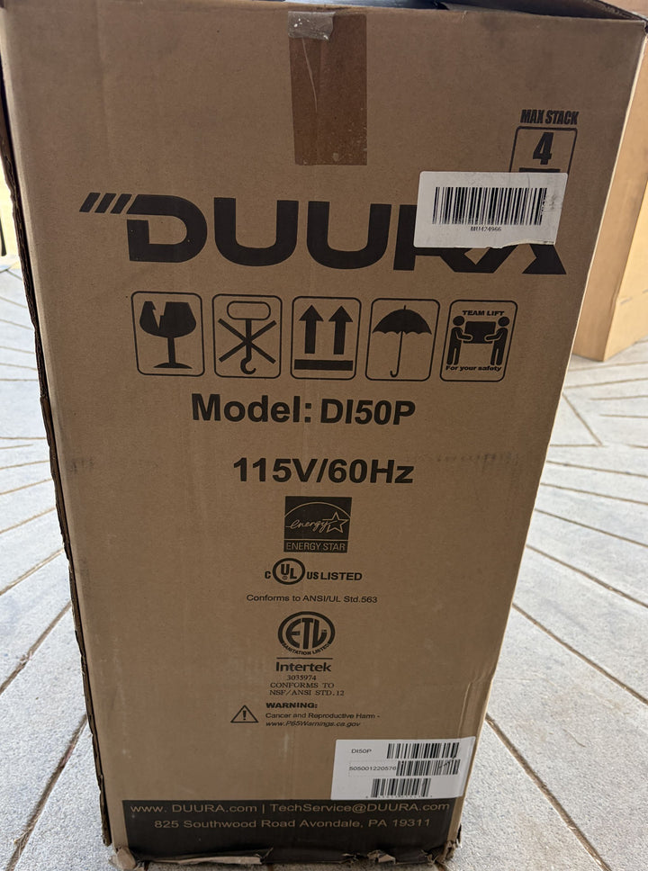 Cardboard packaging box for a Duura D150P ice maker, featuring model number, electrical specifications, handling icons, and certification labels on a brown surface.