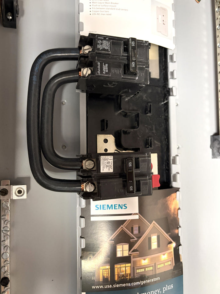 Close-up view of a Siemens electrical panel featuring circuit breakers with thick black cables and a promotional card showing a lit residential house.