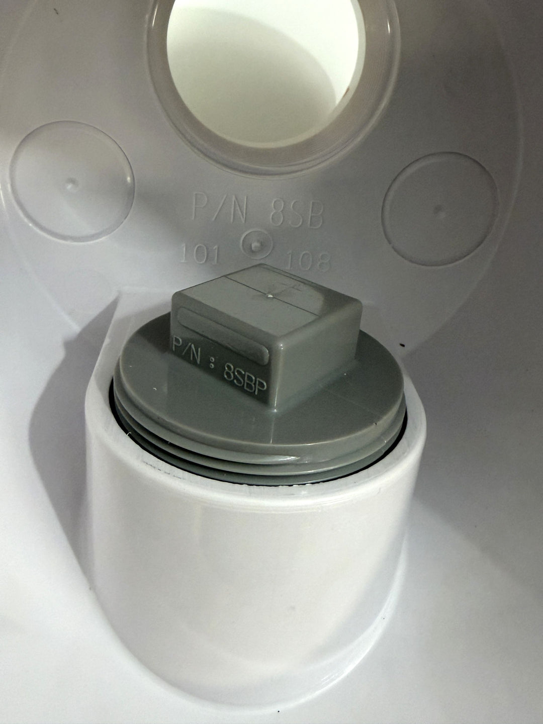 Close-up of a white and gray plastic pool suction outlet drain cover component showing part numbers molded into the surface, highlighting detailed construction from AquaStar.