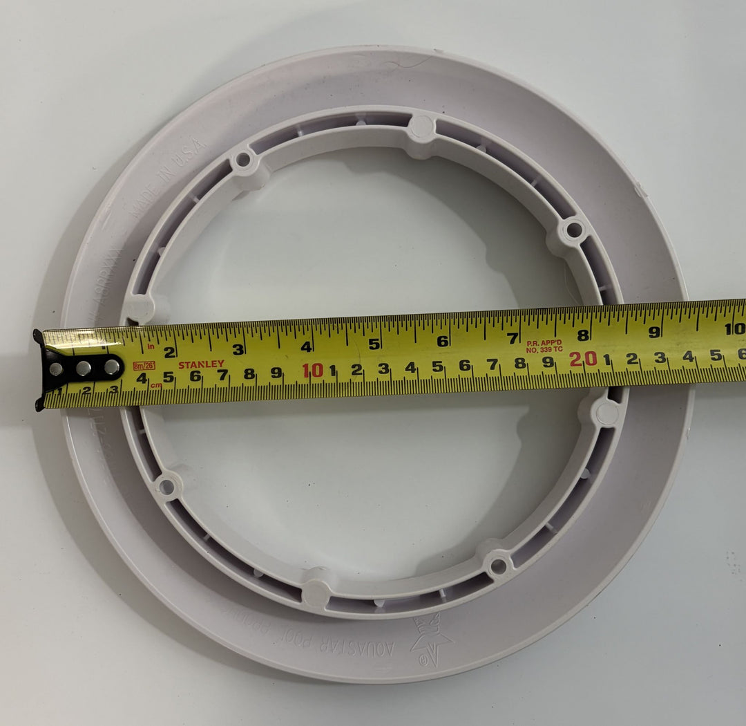 A white round pool drain cover with a built-in mounting ring, shown with a measuring tape across its diameter, featuring AquaStar branding.