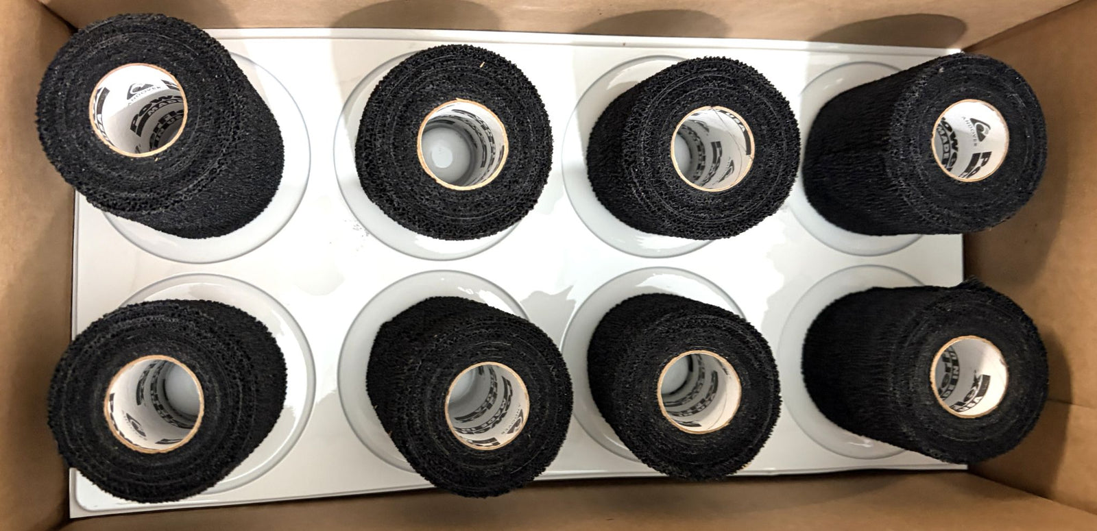 Box containing eight rolls of black sports wrap from Milliken, arranged neatly on a white insert for secure packaging and easy access.